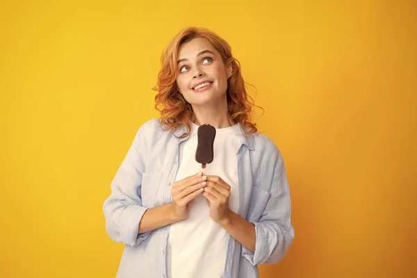 Young woman eat ice creams with chocolate glaze on yellow background. Funny redhead woman with ice cream