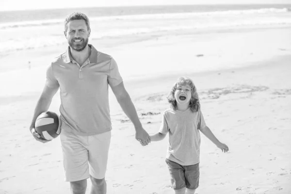 sport activity. smiling father and son walk with ball on beach. daddy with kid boy on summer day. weekend family day. dad and child having fun outdoors. childhood and parenting. family holidays.
