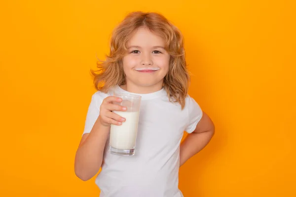 Child with glass of milk on studio yellow background. Kid with milk moustache. Fun portrait of cute child with milk mustache and funny face. Child drink milk