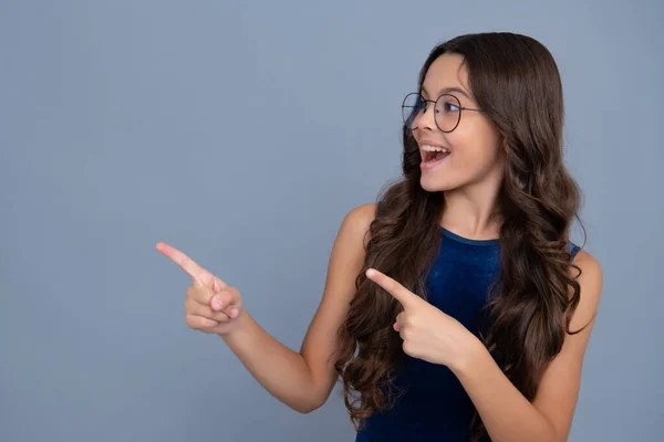 Wow, its unbelievable. Shocked teenager child pointing aside at copy space. Teen girl pointing with two hands and fingers to the side. Happy girl face, positive and smiling emotions