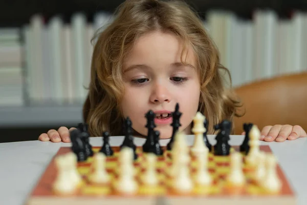 Little child play chess. Kid playing board game. Thinking child brainstorming and idea in chess game. Kids early development. Boy kid playing chess at home. Portrait close up, funny face