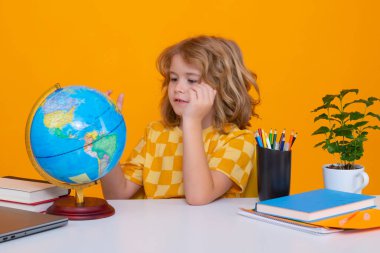 School and education concept. Portrait of cute child school boy looking at globe during geography lesson isolated on yellow studio background. Back to school