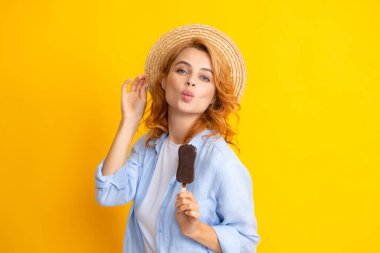 Genç kadın lezzetli dondurma yiyor, dondurulmuş tatlıyı seviyor, günlük kıyafetler giyiyor, sarı arka planda izole edilmiş.