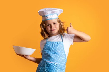 Funny kid chef cook with kitchen plate, studio portrait. Child chef cook prepares food on isolated studio background. Kids cooking. Teen boy with apron and chef hat preparing a healthy meal