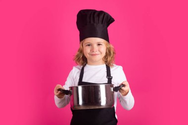 Child chef cook with cooking pot. Kid in cooker uniform and chef hat preparing food on studio color background. Cooking, culinary and kids food concept