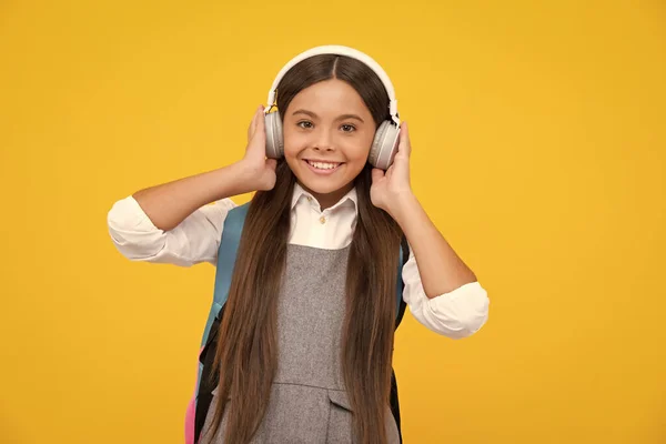 School teenager child girl in headphones with school backpack. Teenager student, isolated background. Learning music. Happy girl face, positive and smiling emotions