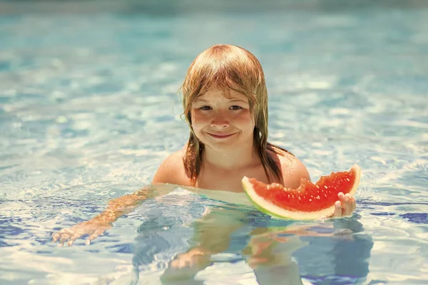 Child with watermelon in swimming pool. Kids eat summer fruit outdoors. Child playing in the swimming pool. Summer kids activity. Little child playing in blue water. Summer watermelon fruit for