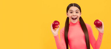 amazed teen girl with red apple on yellow background. Child girl portrait with apple, horizontal poster. Banner header with copy space