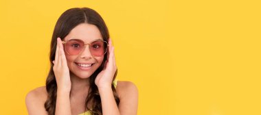 child with long hair in glasses. happy teen girl with curly hair on yellow background. Child face, horizontal poster, teenager girl isolated portrait, banner with copy space