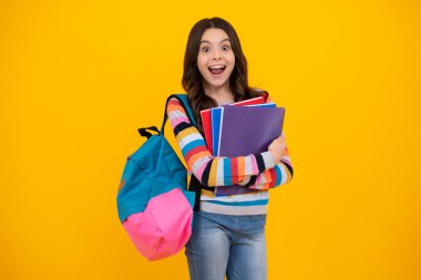 Amazed teenager. School girl hold copybook and book on yellow isolated studio background. School and education concept. Teenager girl in school uniform. Excited teen girl