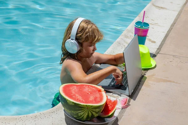 Child work outside with laptop in pool. Kid working on laptop from the swimming pool. Summer business