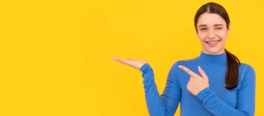winking woman portrait point fingers on copy space yellow background, advertising. Woman isolated face portrait, banner header poster with mockup copyspace
