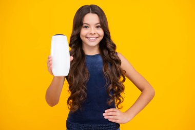 Teenager child girl showing bottle shampoo conditioners or shower gel isolated on yellow background. Hair cosmetic product. Mock up bottle. Happy girl face, positive and smiling emotions