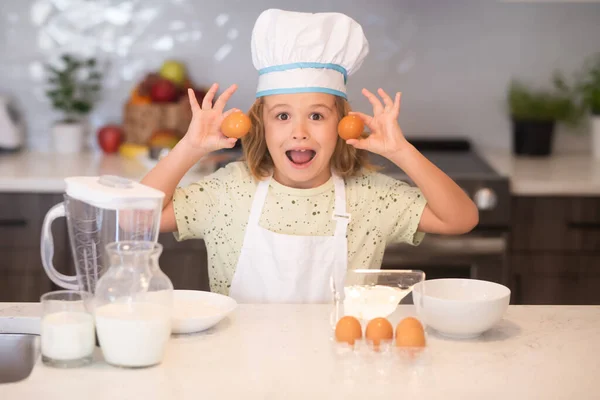 Child chef cook with eggs. Kid chef cook wearing cooker uniform and chef hat preparing food on kitchen. Cooking, culinary and kids food concept