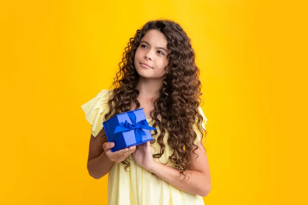 Child with gift present box on isolated yellow background. Presents for birthday, Valentines day, New Year or Christmas. Thinking face, thoughtful emotions of teenager girl