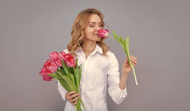 Gri arka planda bahar lale çiçekleri olan gülümseyen sarışın kadın..