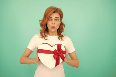 Şaşırmış kız mavi arka planda hediye kutusunu tutuyor..