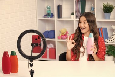Çocuk vlogcusu saç kremi ya da şampuan şişesi ile telefonda video blogu yapıyor. Web günlüğü ve vlog. Genç kız blogger etkileyicisi sosyal medya için video kaydediyor