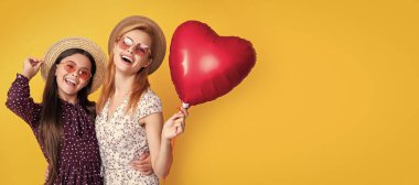 Anne ve kız çocuk afişi, kopyalama alanı, izole bir arka plan. Anne ve kızı gülümsüyor. Sarı arka planda aşk balonu tutuyorlar.