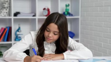 serious child writing in notebook concentrated on homework with smile, exam preparing.