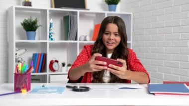 Happy girl win smartphone game making yes gesture at school desk, playing.