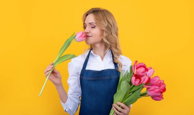 happy girl in apron with spring tulip flowers on yellow background.
