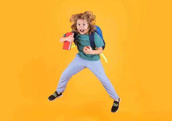 Funny child school boy jumping on a yellow studio background