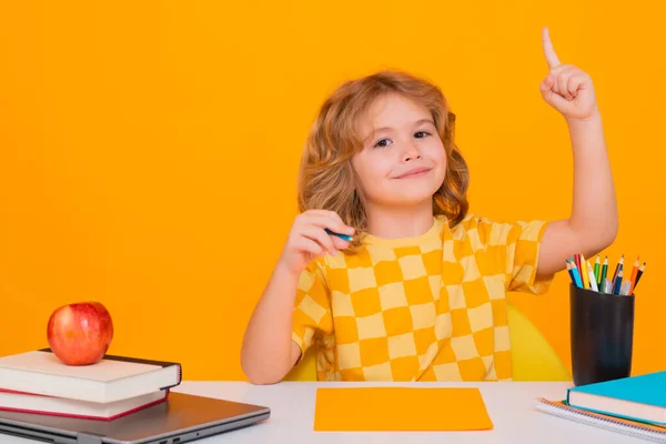 School kid holding index finger up with great new idea. School child portrait isolated on yellow studio background. Kid boy from elementary school. Pupil go study. Clever schoolboy learning