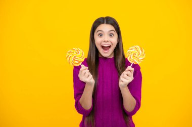 Excited face. Child eat lollipop popsicle over yellow isolated background. Yummy caramel, candy shop. Amazed expression, cheerful and glad