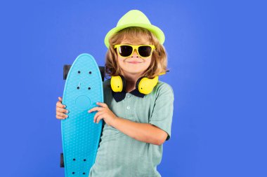 Happy child boy holding skateboard over blue background isolated. Studio portrait of fashion kids