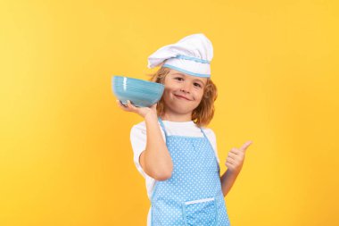 Kid chef cook with cooking bowl. Child wearing cooker uniform and chef hat preparing food on kitchen, studio portrait. Cooking, culinary and kids food concept