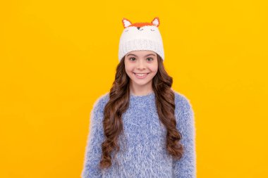 happy teen girl in knitwear on yellow background. portrait of child wearing warm clothes. express positive emotion. winter fashion. kid with curly hair in hat. female fashion model.