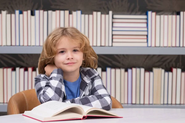 School child studying in school library. Portrait of child reading in library on background with books