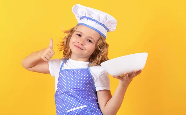Funny kid chef cook with kitchen plate, studio portrait. Child chef cook. Child wearing cooker uniform and chef hat preparing food, studio portrait