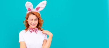 happy winking easter girl in bunny ears and bow tie on blue background. Woman isolated face portrait, banner with mock up copyspace