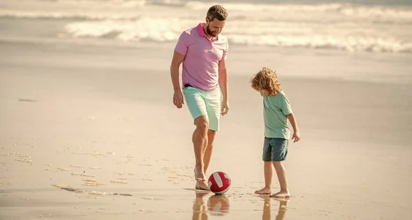 childhood and parenting. family holidays. sport activity. father and son play football on beach. daddy with kid boy on warm day. weekend family day. dad and child having fun outdoors.
