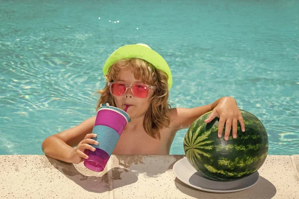 Funny kid in swimming pool. Child drink cocktail, summer fruits, watermelon. Summer cocktail for children
