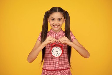 Portrait of teenage girl with clock alrm, time and deadline. Studio shot isolated on yellow background. Happy teenager, positive and smiling emotions of teen girl