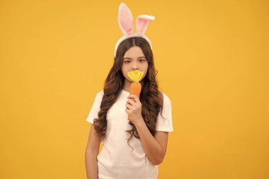 Tavşan kulaklı çocuk sarı arka planda havuç tutuyor, Paskalya.