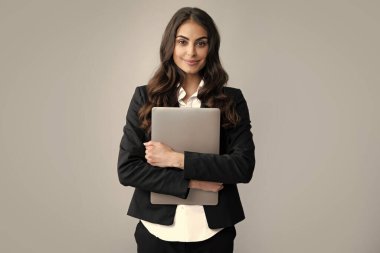 Gri duvarda dizüstü bilgisayarı olan neşeli bir iş kadını. Gri arka planda dizüstü bilgisayarı olan güzel, çekici, şık ve zeki bir kadının portresi.