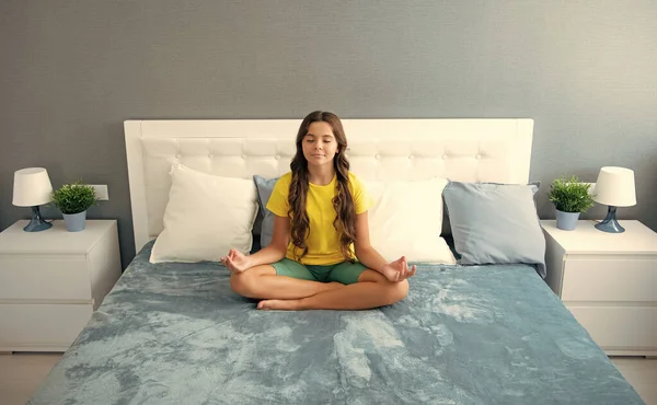 Morning Meditation on bed. Teenager child practicing meditation at bedroom. Relaxed girl on bed in lotus pose and meditating