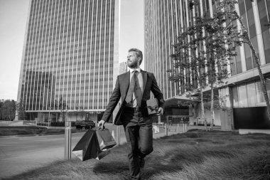 İş adamı kılığındaki mutlu girişimci alışveriş çantası ve hediye kutusunu ofisin dışında tutuyor, erkekler günü..