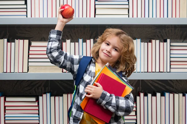School boy with books and apple in library. Back to school. Funny little boy from elementary school with book. Education