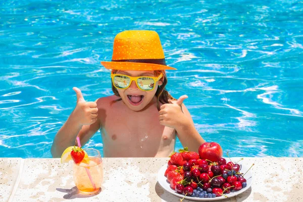 Child eating fruits near swimming pool during summer holidays. Kids eat fruit outdoors. Healthy fruits for children