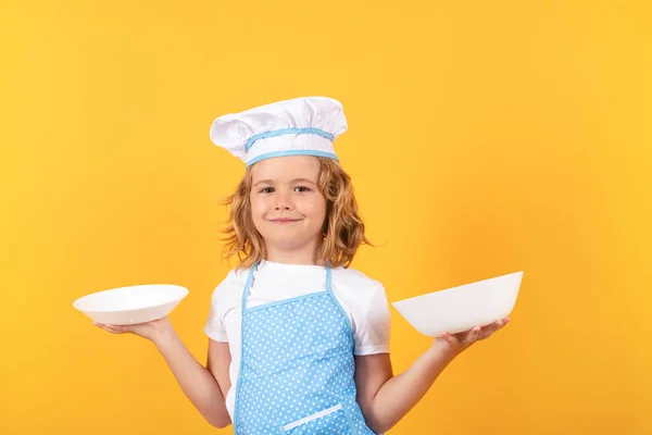 Funny kid chef cook with kitchen plate, studio portrait. Chef kid boy making healthy food. Portrait of little child in chef hat isolated on studio background. Child chef. Cooking process