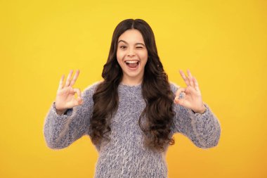 Funny teen child over yellow background doing ok gesture and winking with hand smiling with happy face. Amazed teenager. Excited teen girl