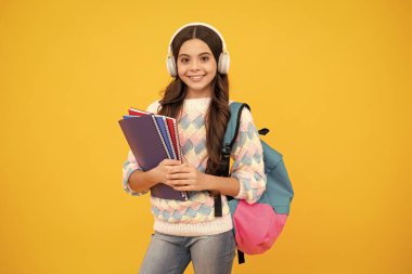 Liseli kız, kulaklıklı genç kız öğrenci, sarı izole stüdyo geçmişiyle ilgili kitaplar tutuyor. Okul ve müzik eğitimi kavramı