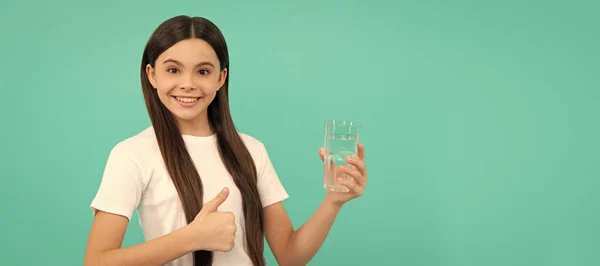 happy teen girl drink water keep daily water balance in body show thumb up, daily water. Banner of child girl with glass of water, studio portrait with copy space
