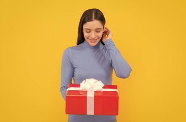 smiling girl holding gift box after shopping on yellow backdrop, purchase.