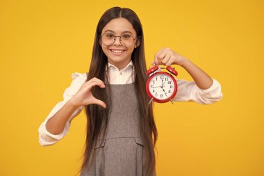 Child teenager girl with alrm clock isolated on yellow background. Time and deadline concept. Happy face, positive and smiling emotions of teenager girl